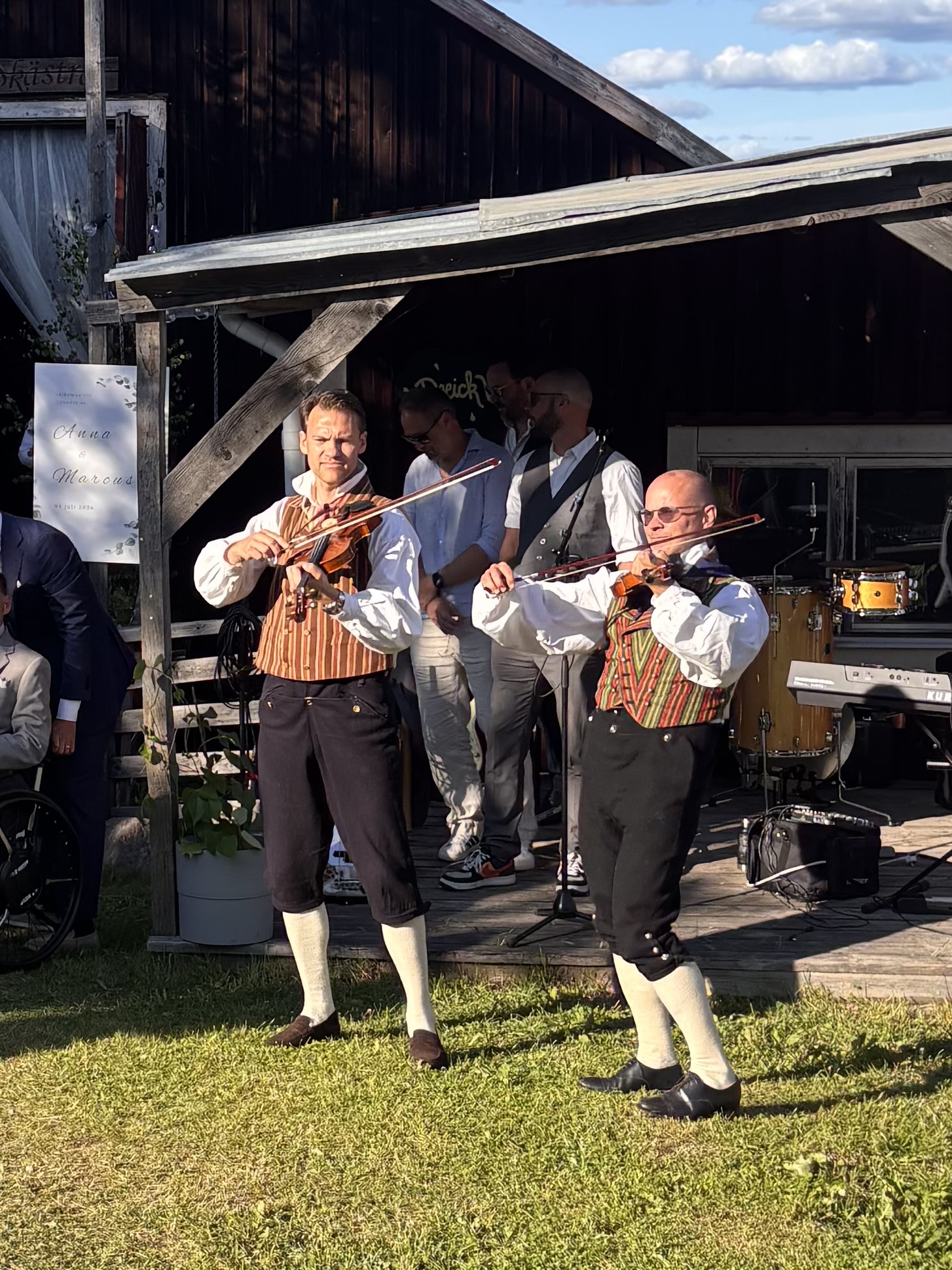 Två spelmän i folkdräkt spelar fiol utomhus
