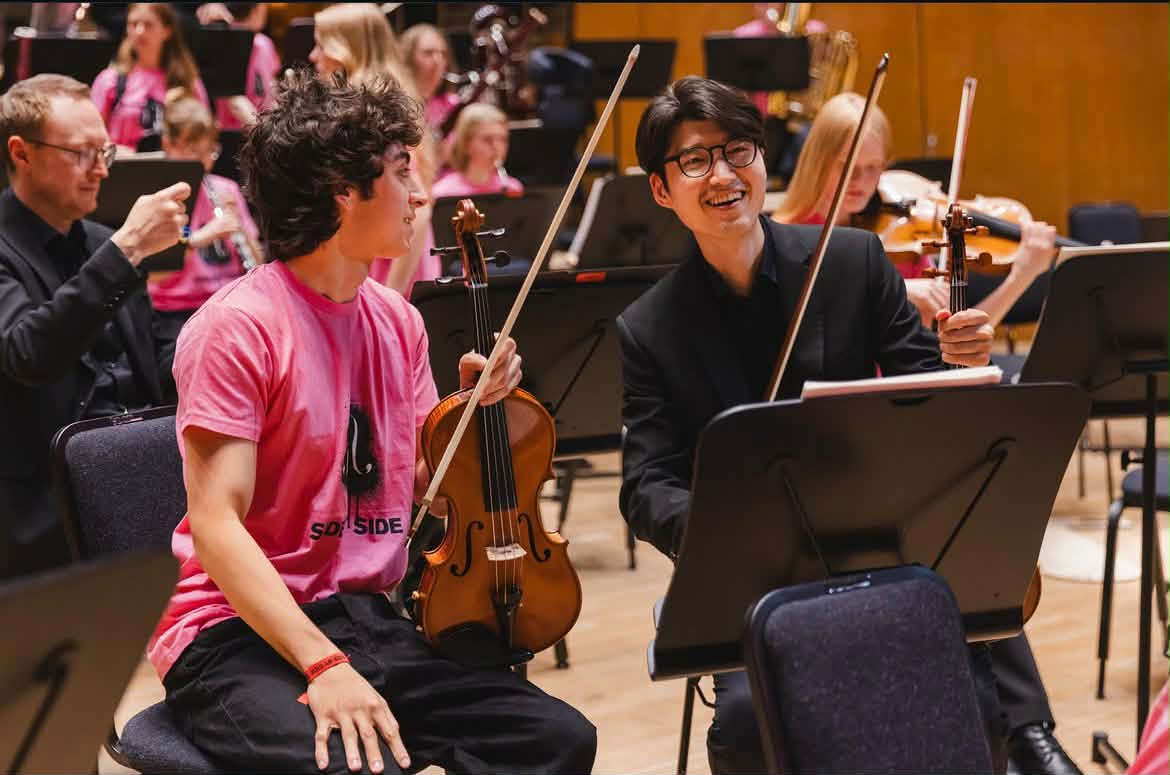 Två violinister samtalar under en orkesterrepetition